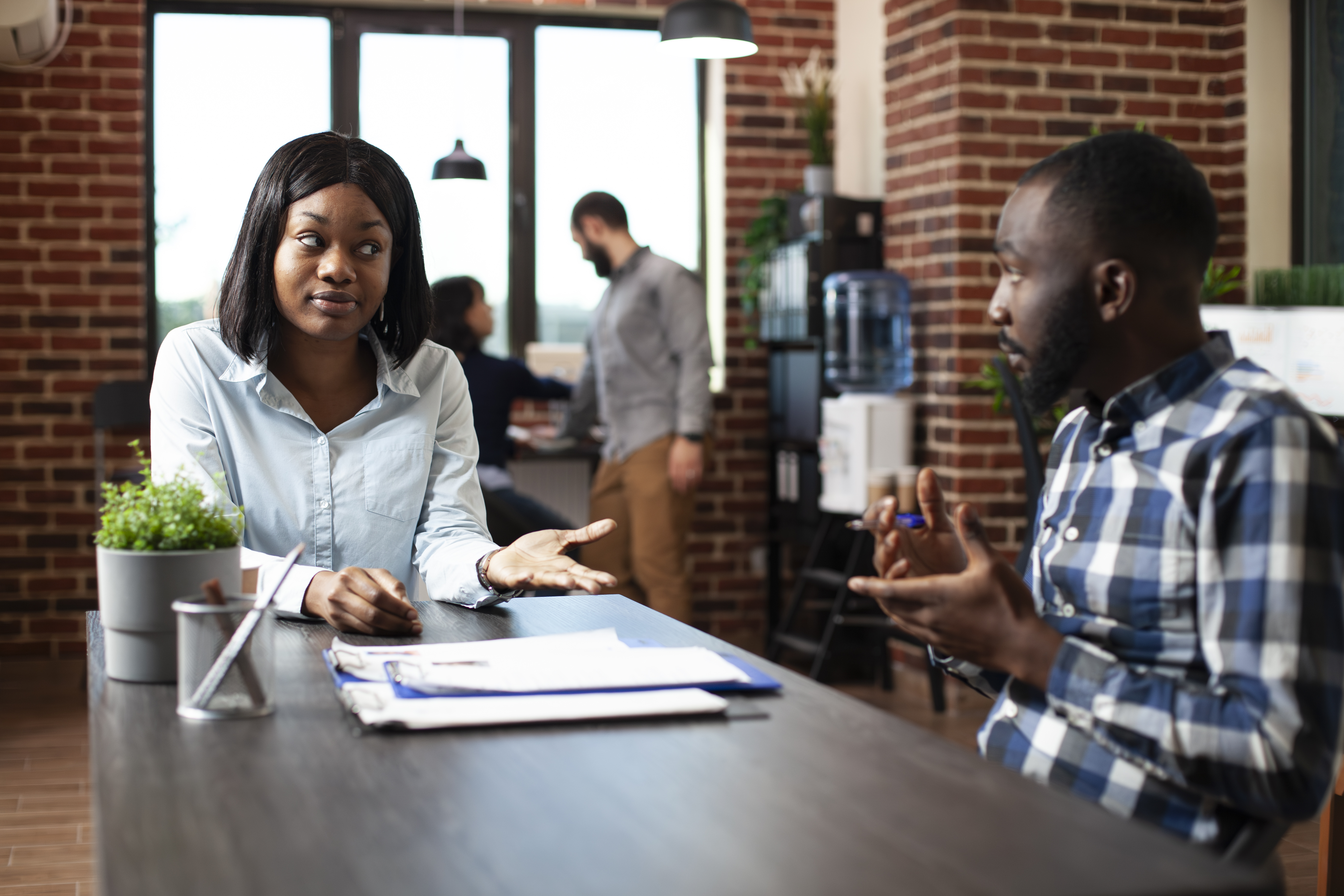 Young black woman explaining her work experiences and expectations to professional hiring manager. Male recruiter and female candidate engage in a formal discussion in a modern office.